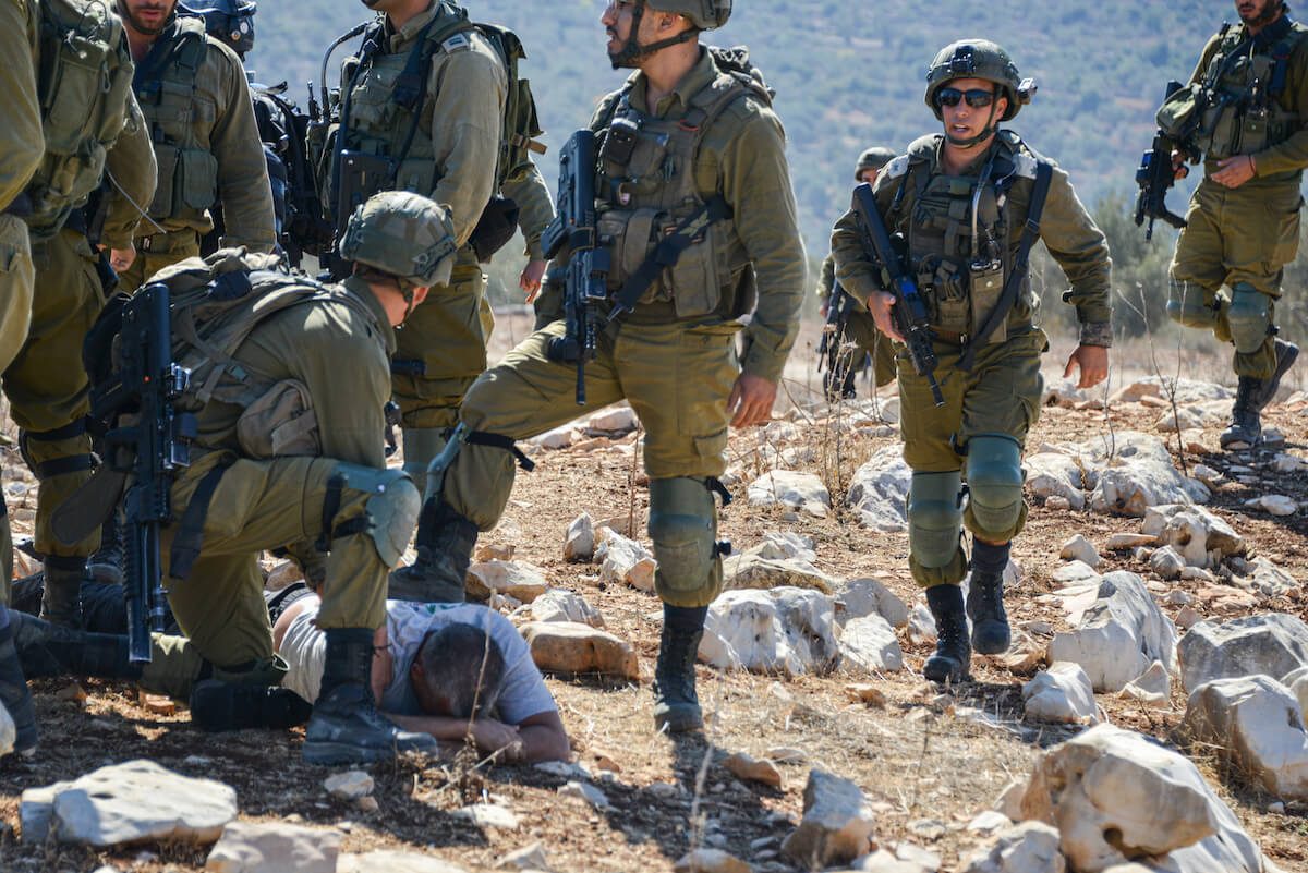 Soldiers on a rocky hillside restraining a man on the ground